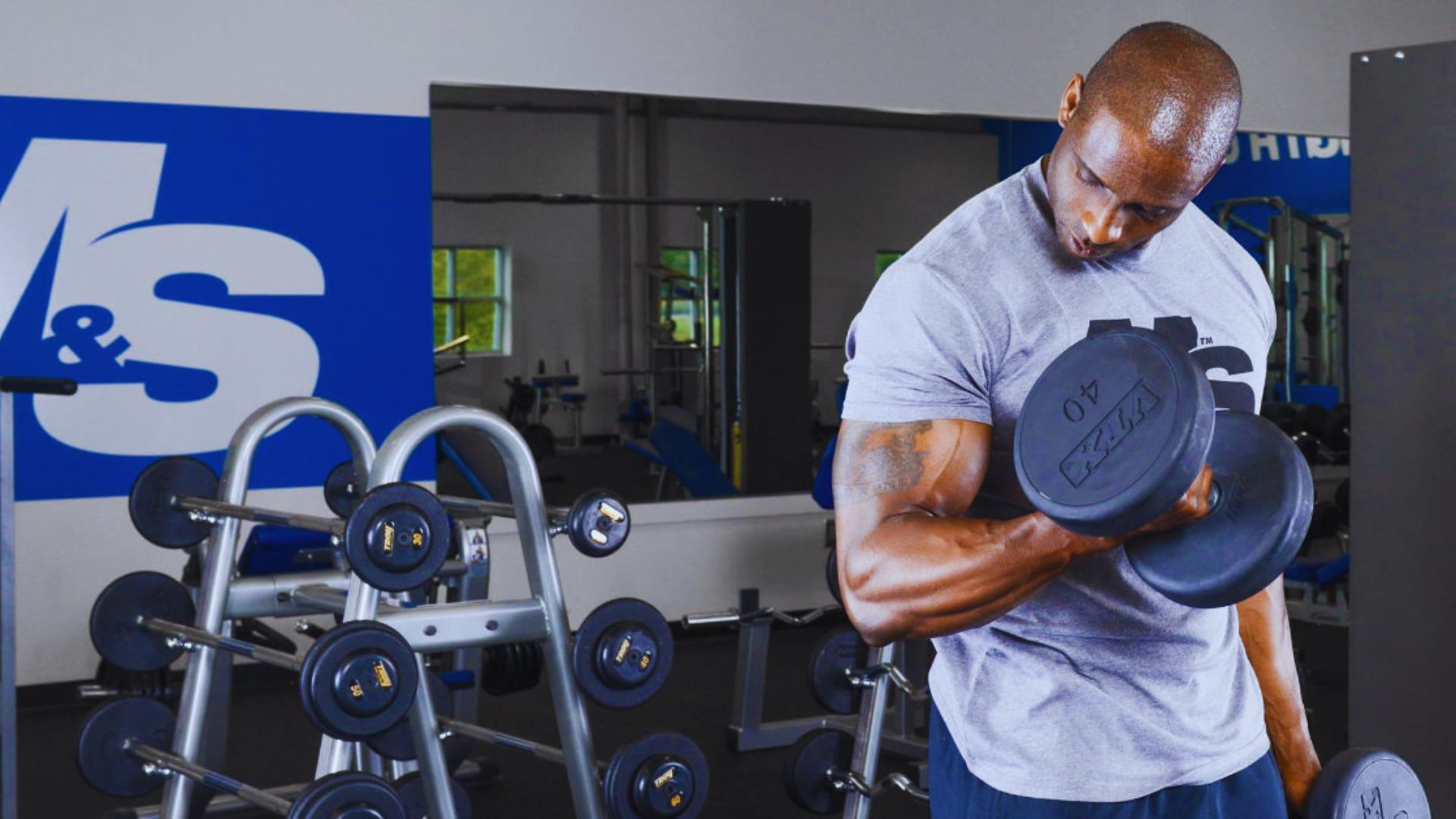 A man is lifting weights in a gym, focusing on his form while surrounded by exercise equipment.