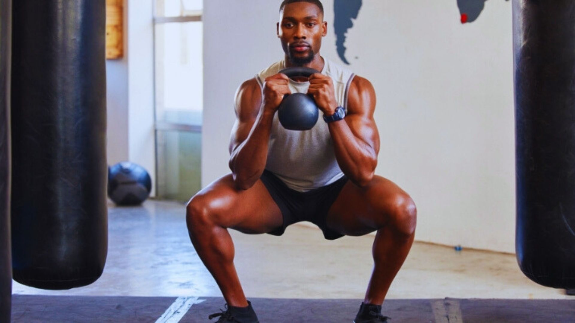 A man performs a goblet squat with a kettlebell in a gym, focusing on his form and strength training.