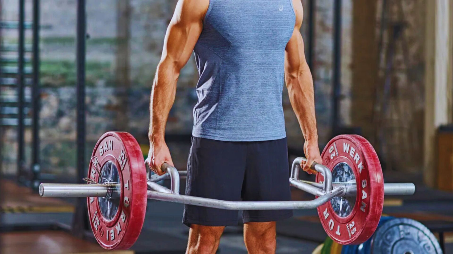 A man performs a trap bar squat, lifting a barbell in a gym setting.