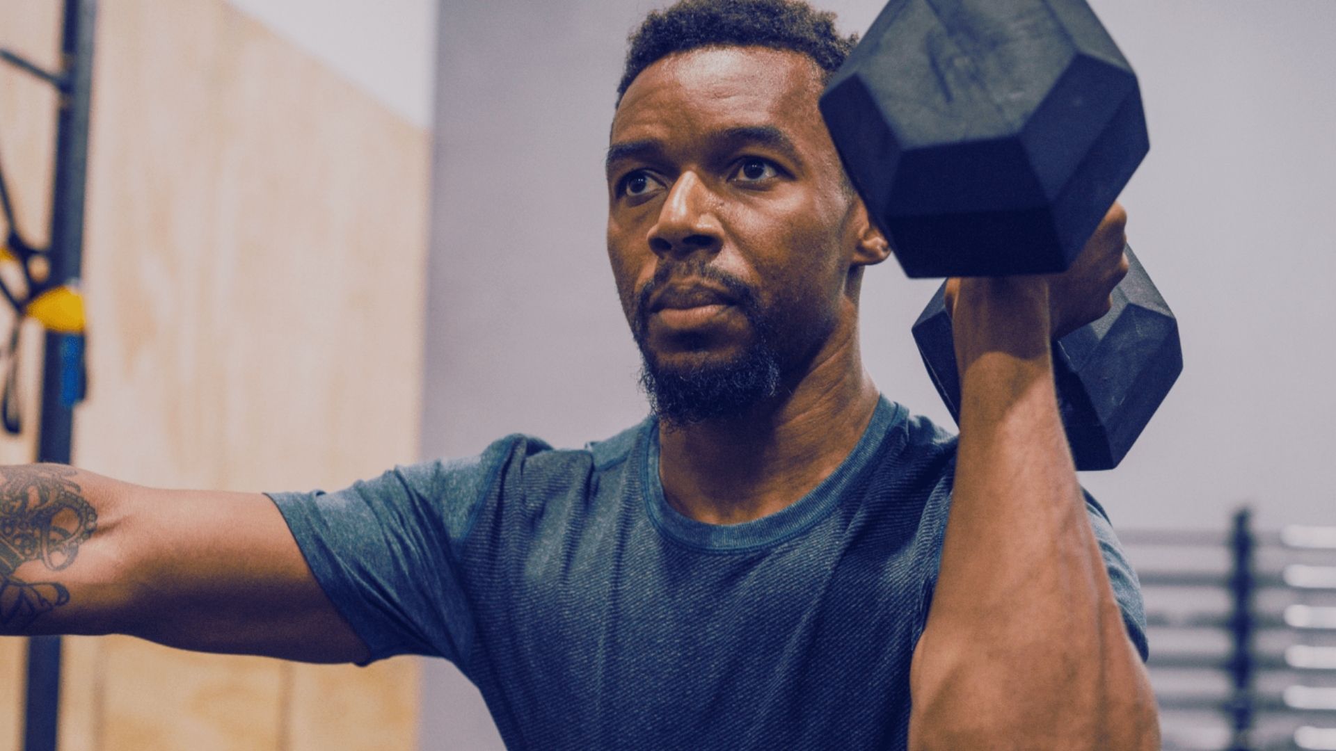 A man performs a power clean with a dumbbell in a gym, demonstrating focus and strength during his workout.