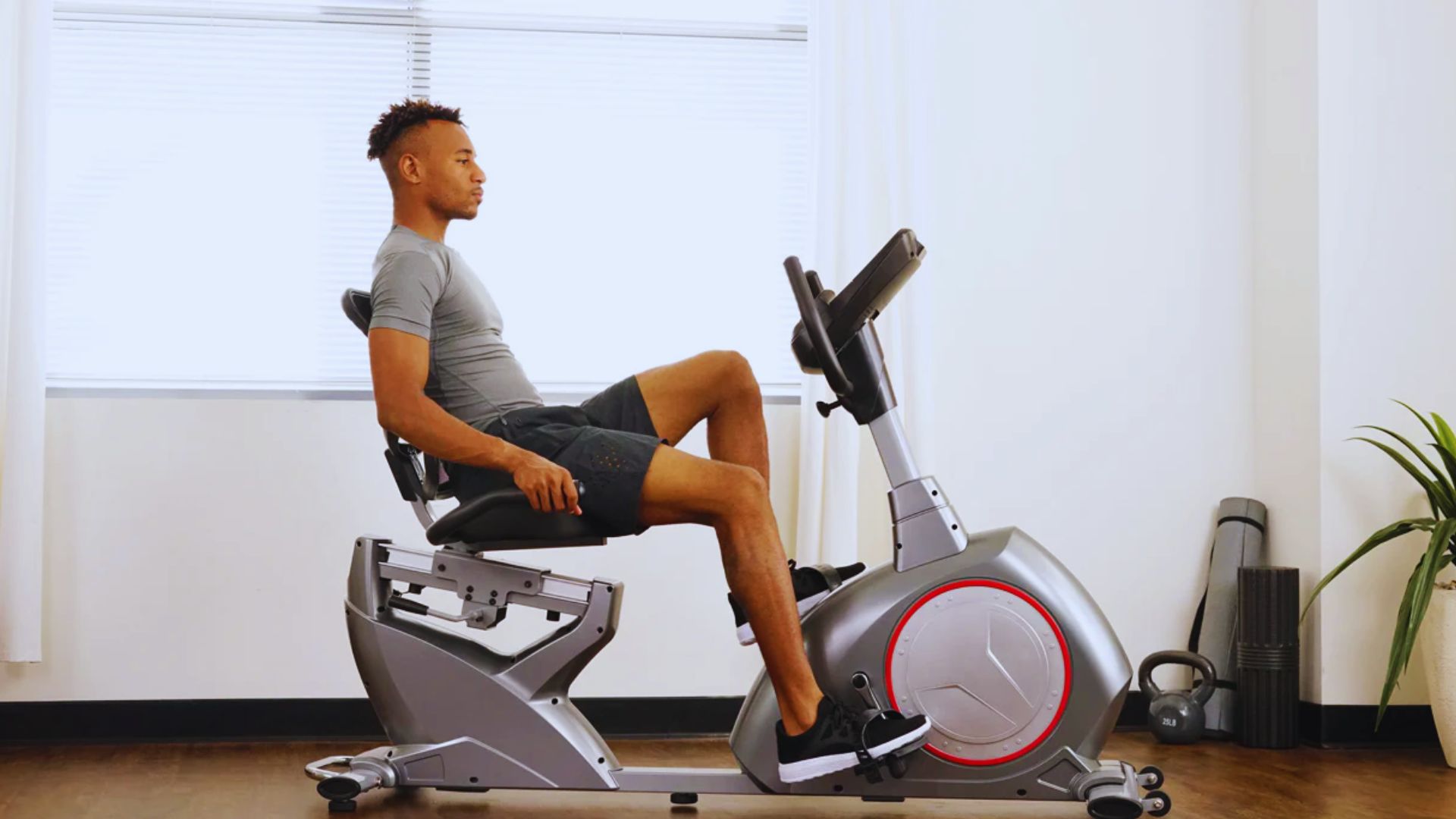 A man is seated on a stationary bike, focused on his workout in a well-lit exercise room.