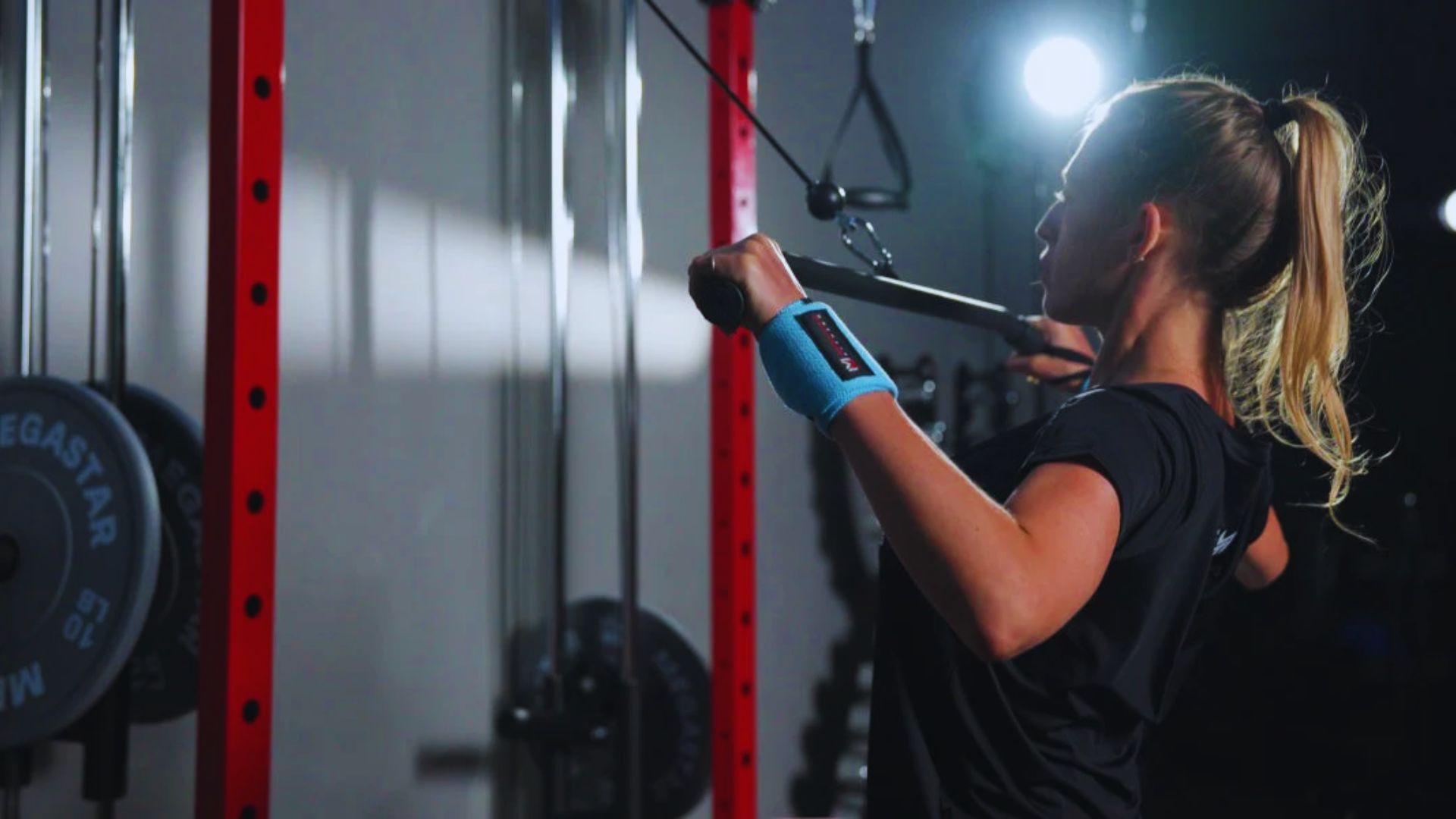 A woman lifts a barbell in a gym, focusing on her workout amidst exercise equipment.