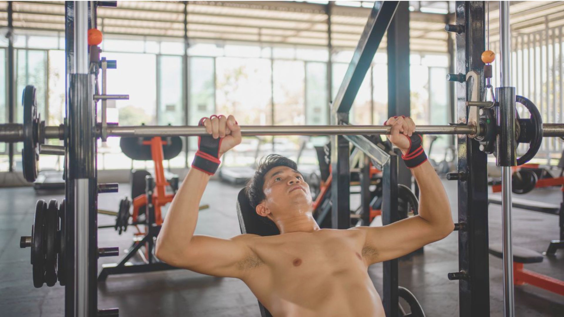 A man performs an exercise on a bar in a gym, showcasing strength and focus during his workout.