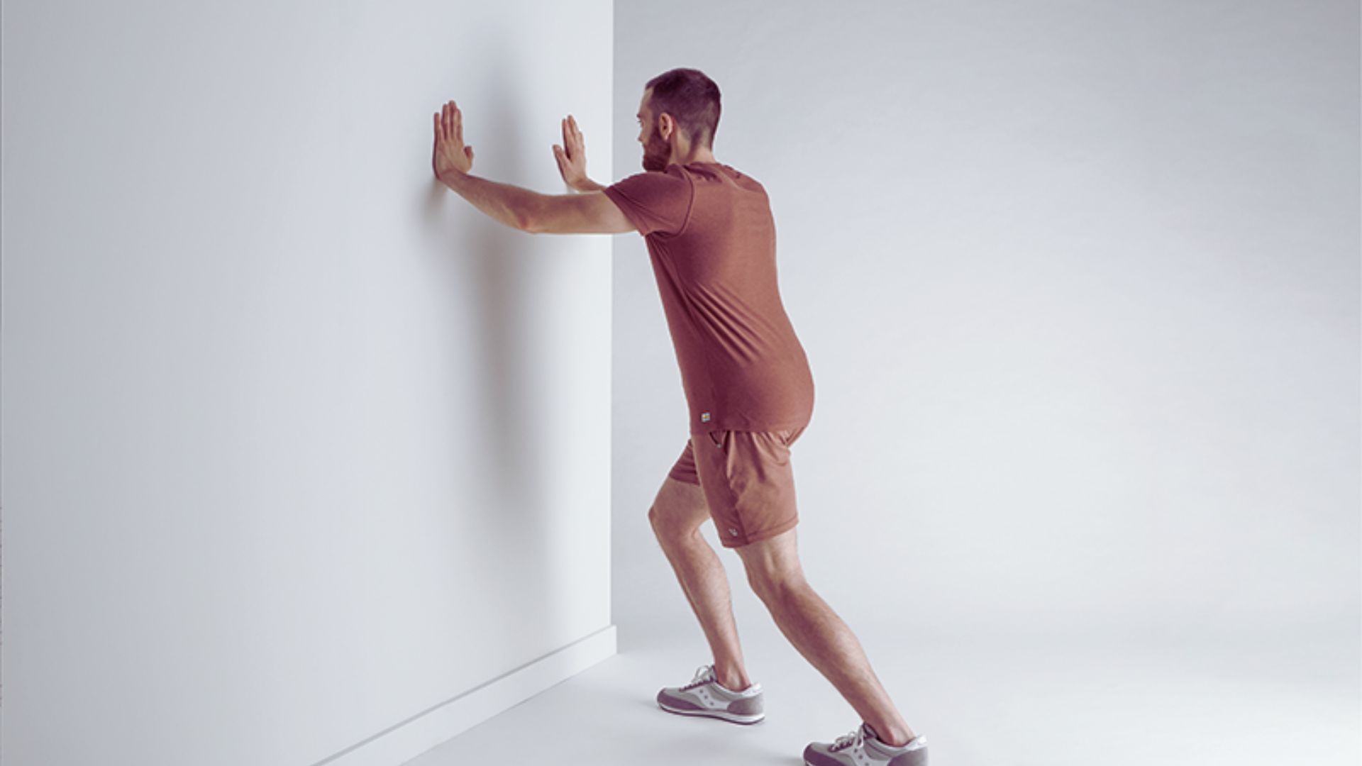A man leans against a wall in a room, appearing relaxed and contemplative.