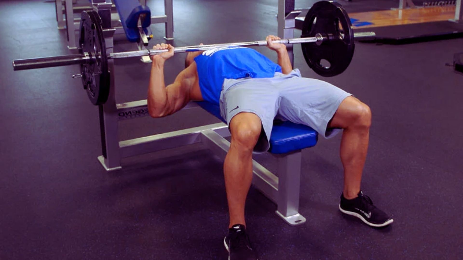 A man performs a bench press in a gym, focusing on strength training with a power bar.