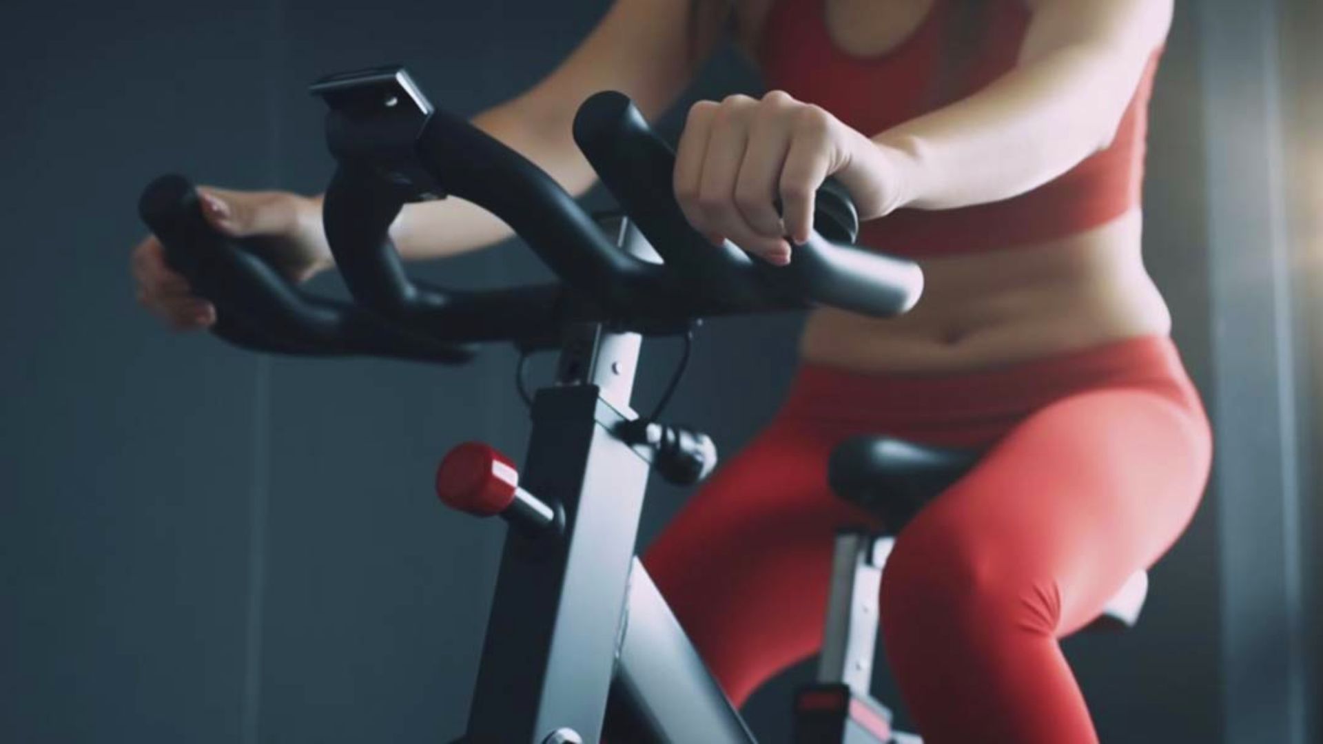 A woman in red pants is pedaling on an exercise bike in a fitness setting.