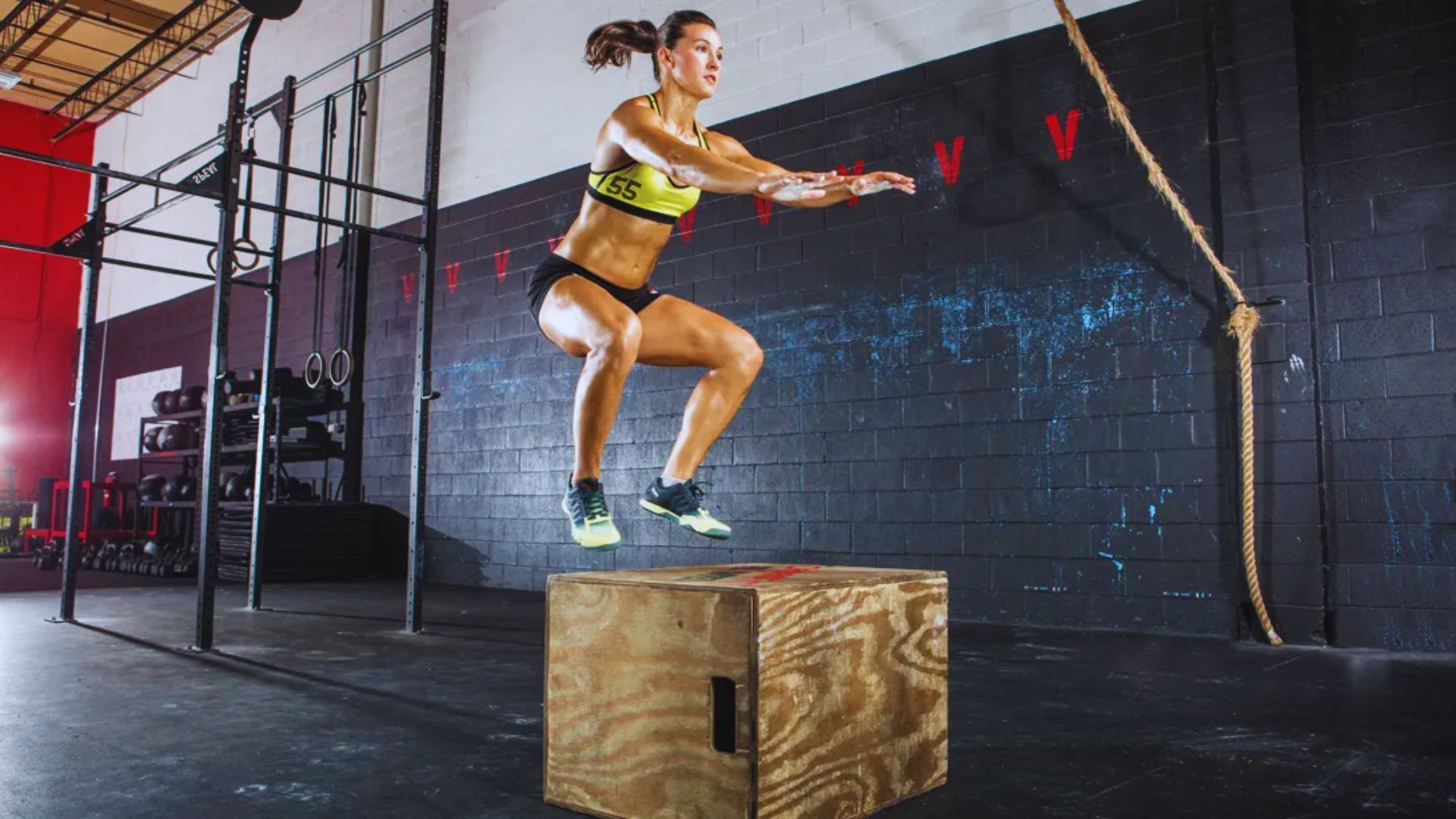 A woman executing a box jump in a gym, highlighting her physical fitness and dynamic movement during training.