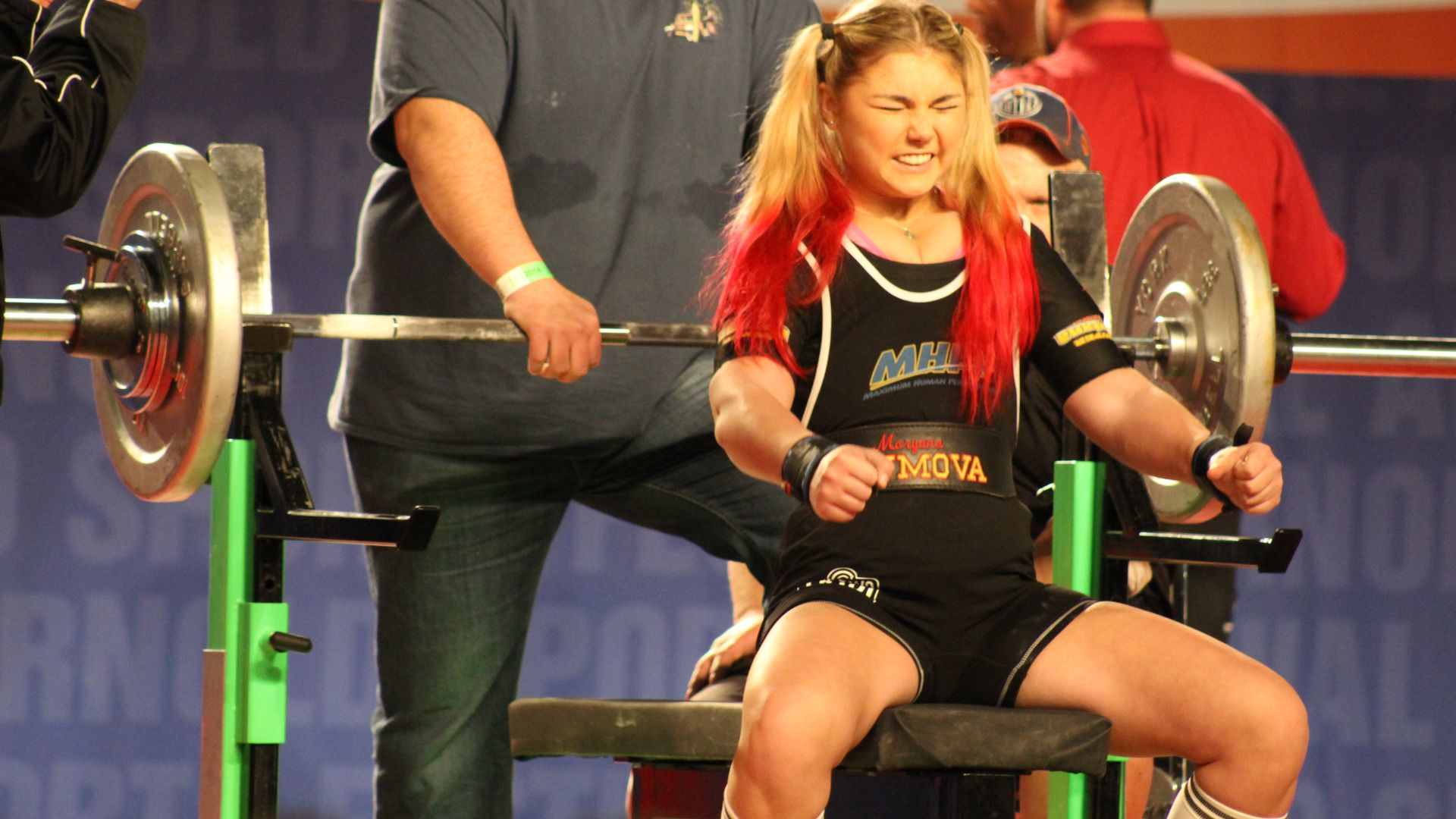 A woman with red hair squats on a bench, demonstrating a fitness pose related to strength training.
