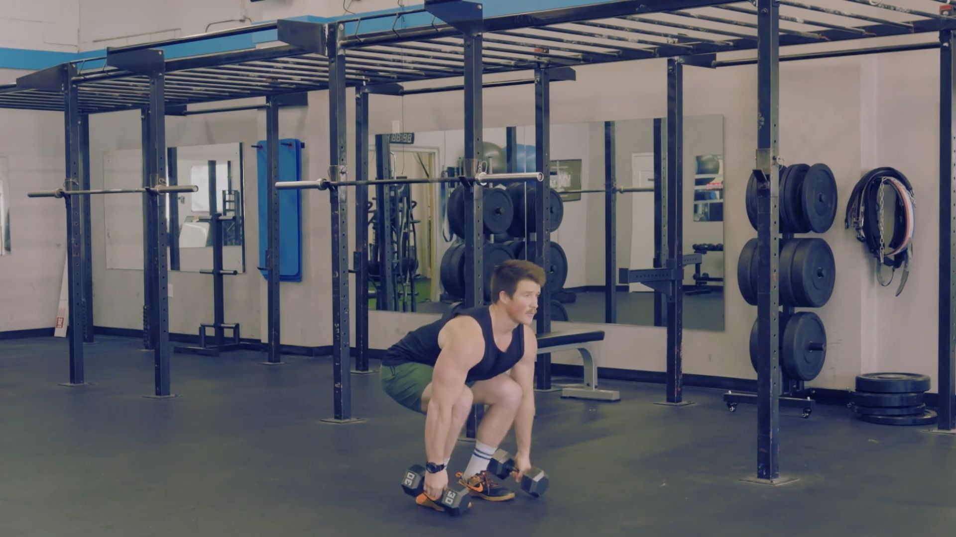 A man squats on a barbell in a gym, preparing to perform a power clean exercise.