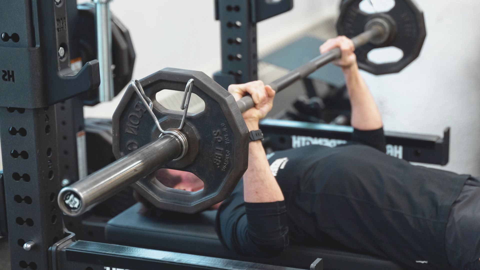 A man lying on a bench performs a chest press with a barbell above him.