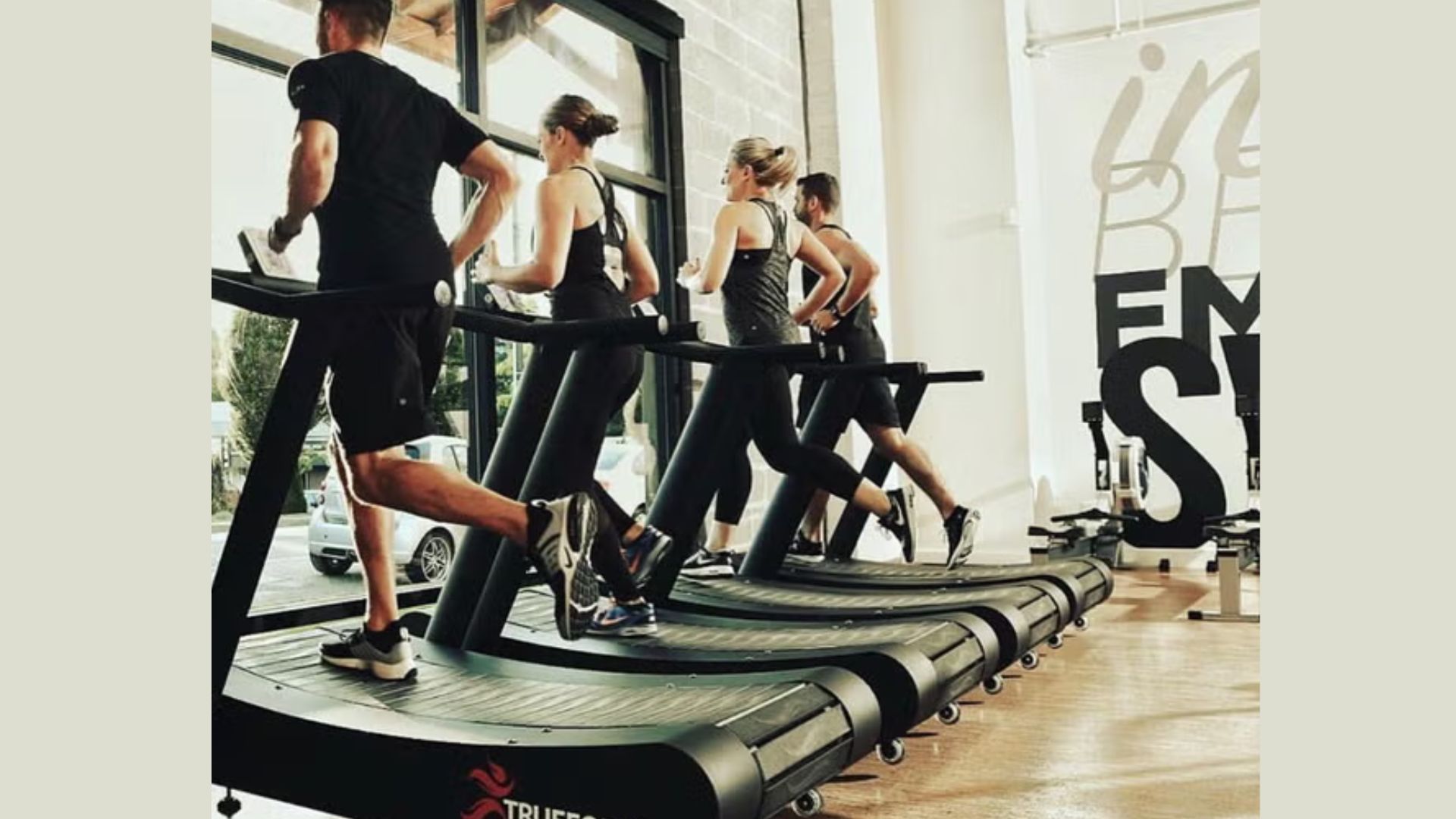 A group of diverse individuals running on treadmills in a modern gym setting, focused on their fitness routines.