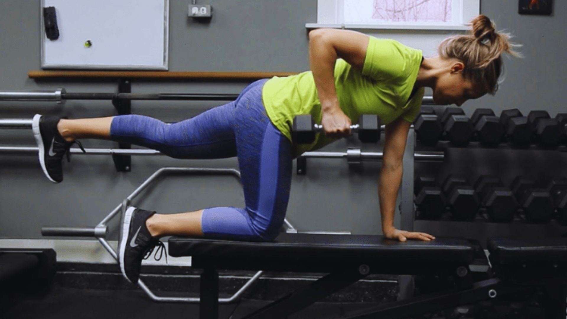 A woman performs a push-up while holding a dumbbell in her right hand, showcasing strength and fitness.