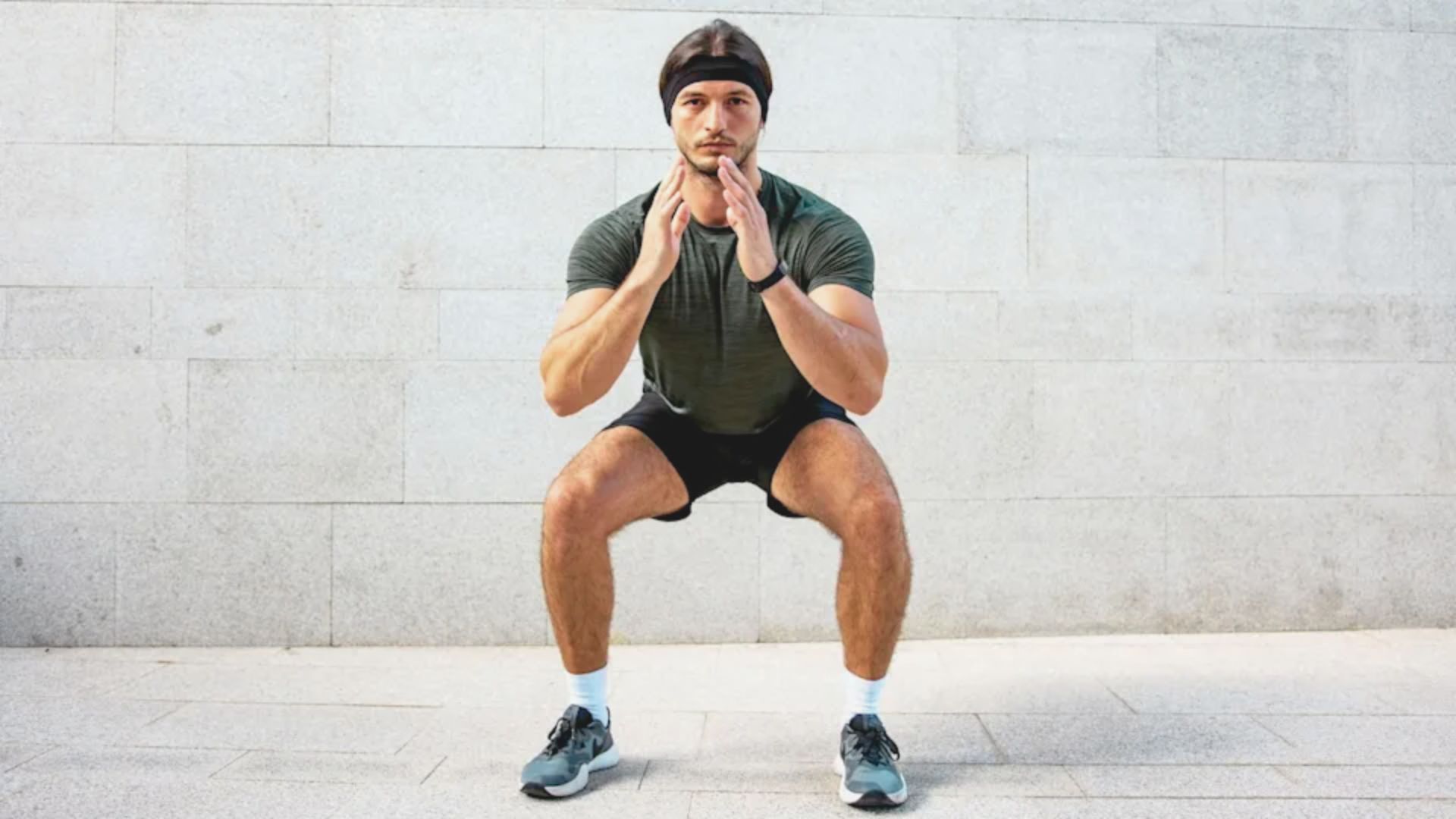 A man performing a sumo squat on the ground, demonstrating the difference between sumo and regular squats.