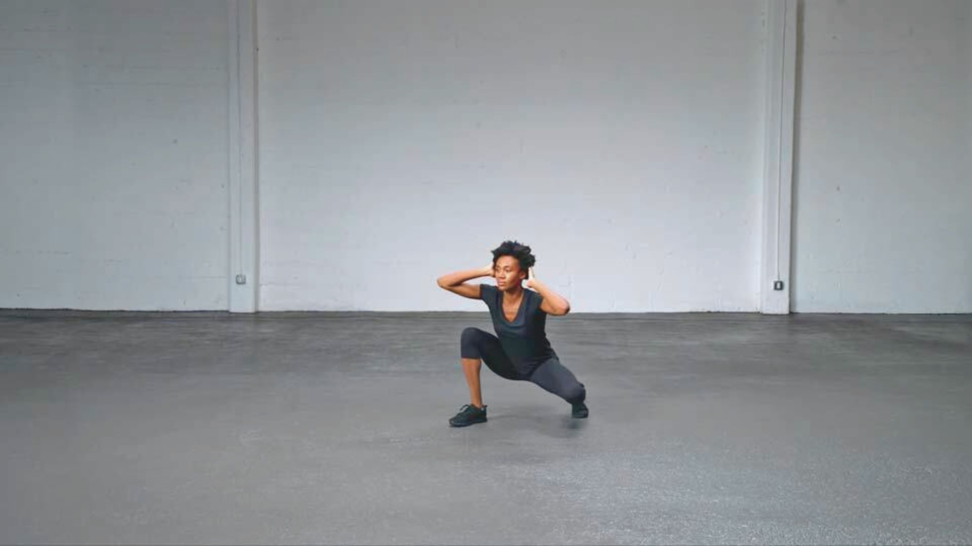 In an empty room, a woman is engaged in a squat exercise, demonstrating strength and concentration.