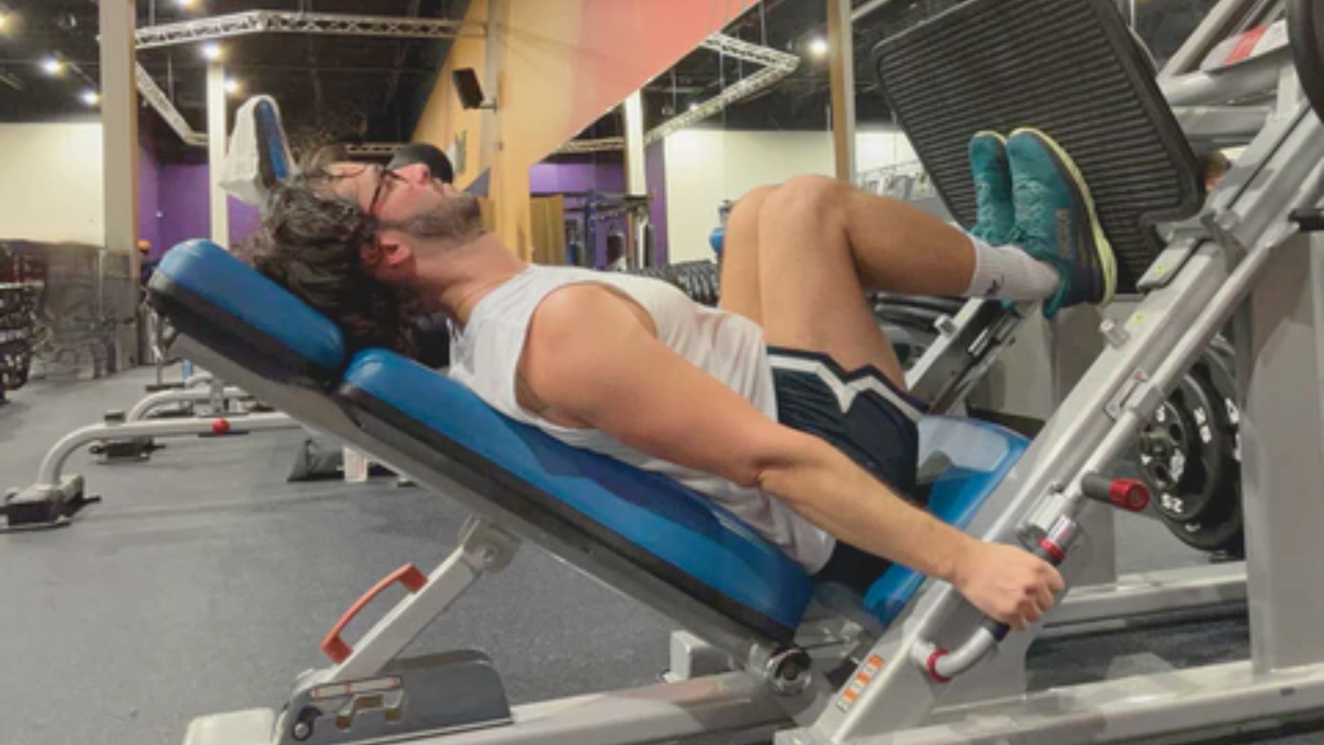 A man is seated on a bench inside a gym, surrounded by exercise equipment.