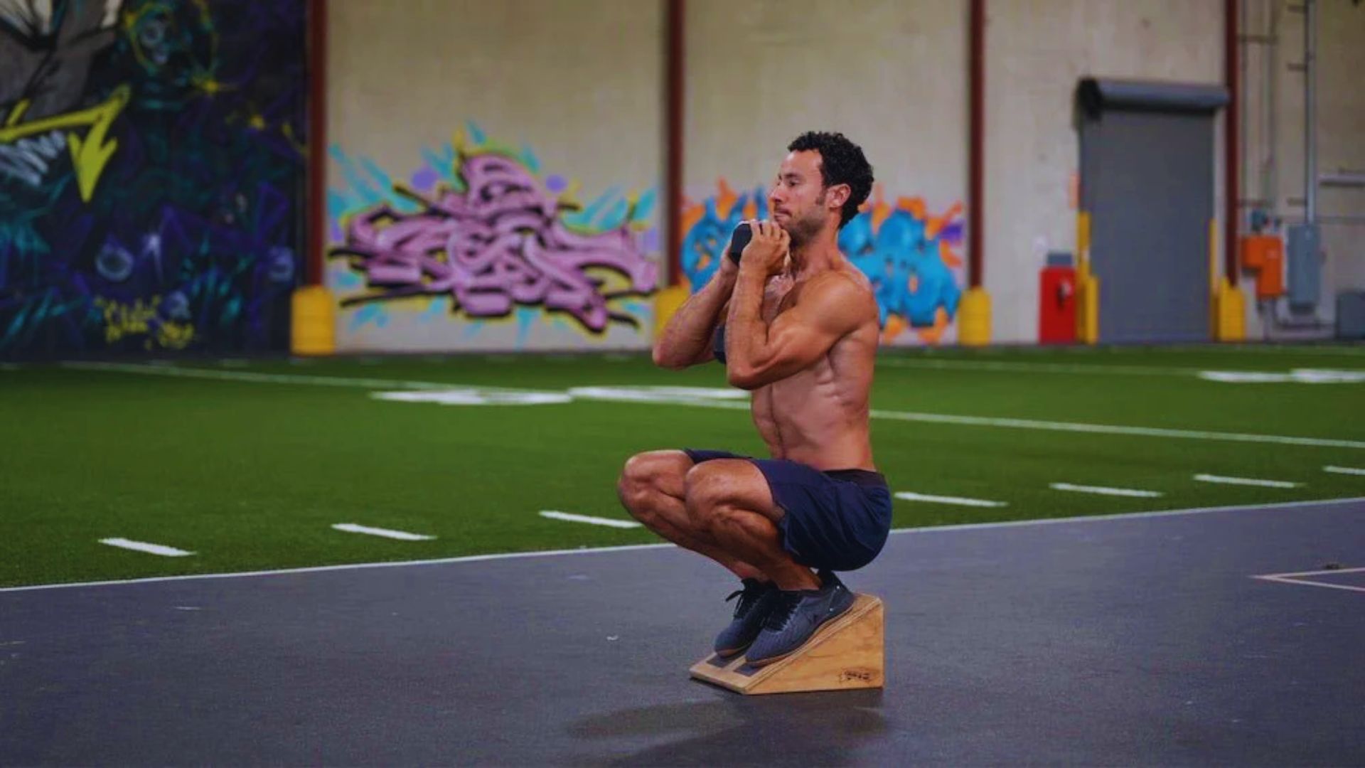 2. In an indoor gym, a man performs a squat on a wooden box, demonstrating strength and balance.