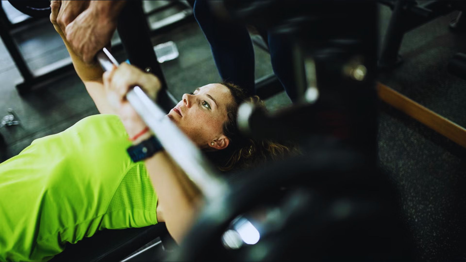A woman performs a bench press in a gym, focusing on her form and technique for safe lifting.