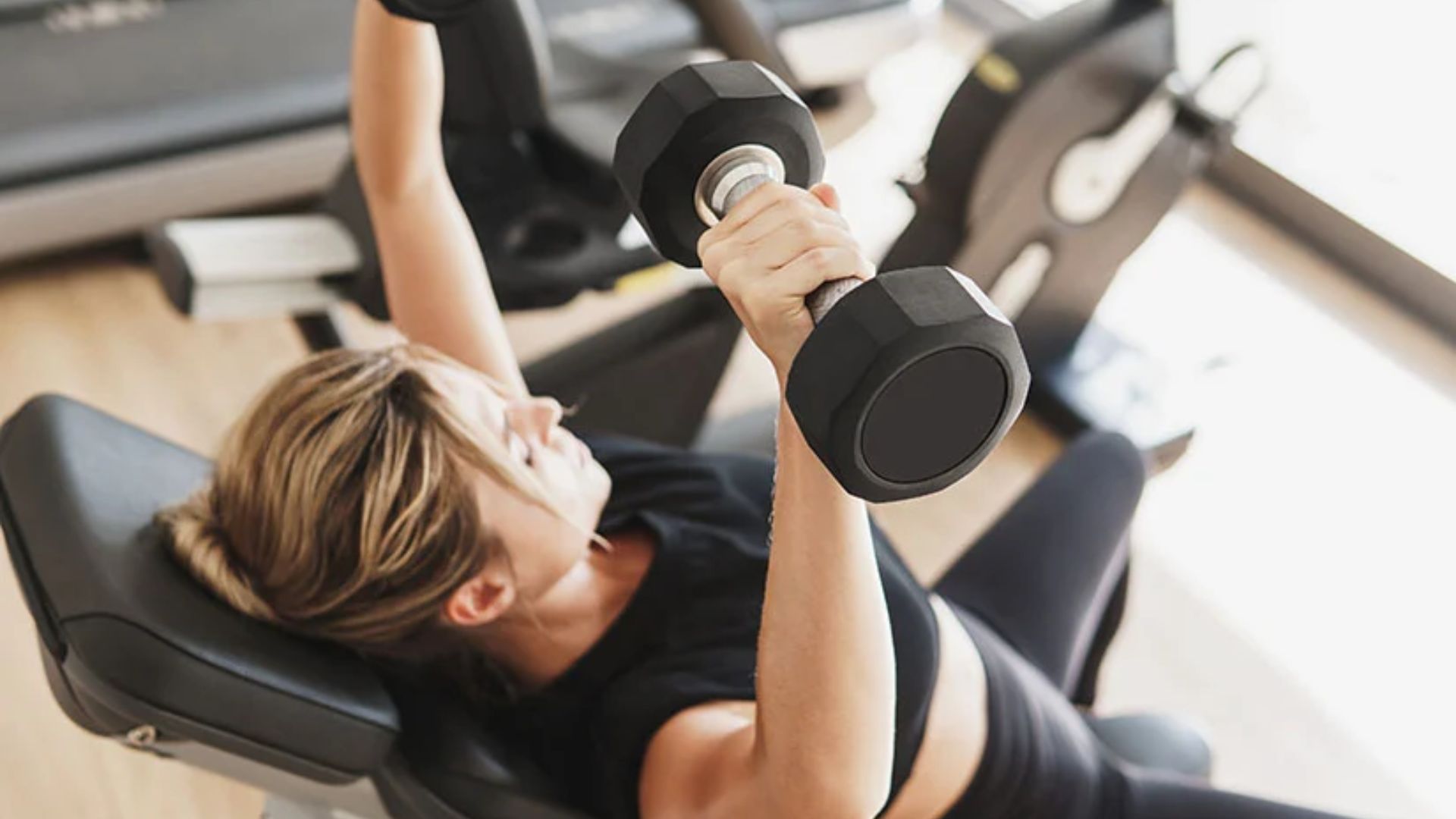 A woman is lifting weights in a gym, focusing on her strength training routine.