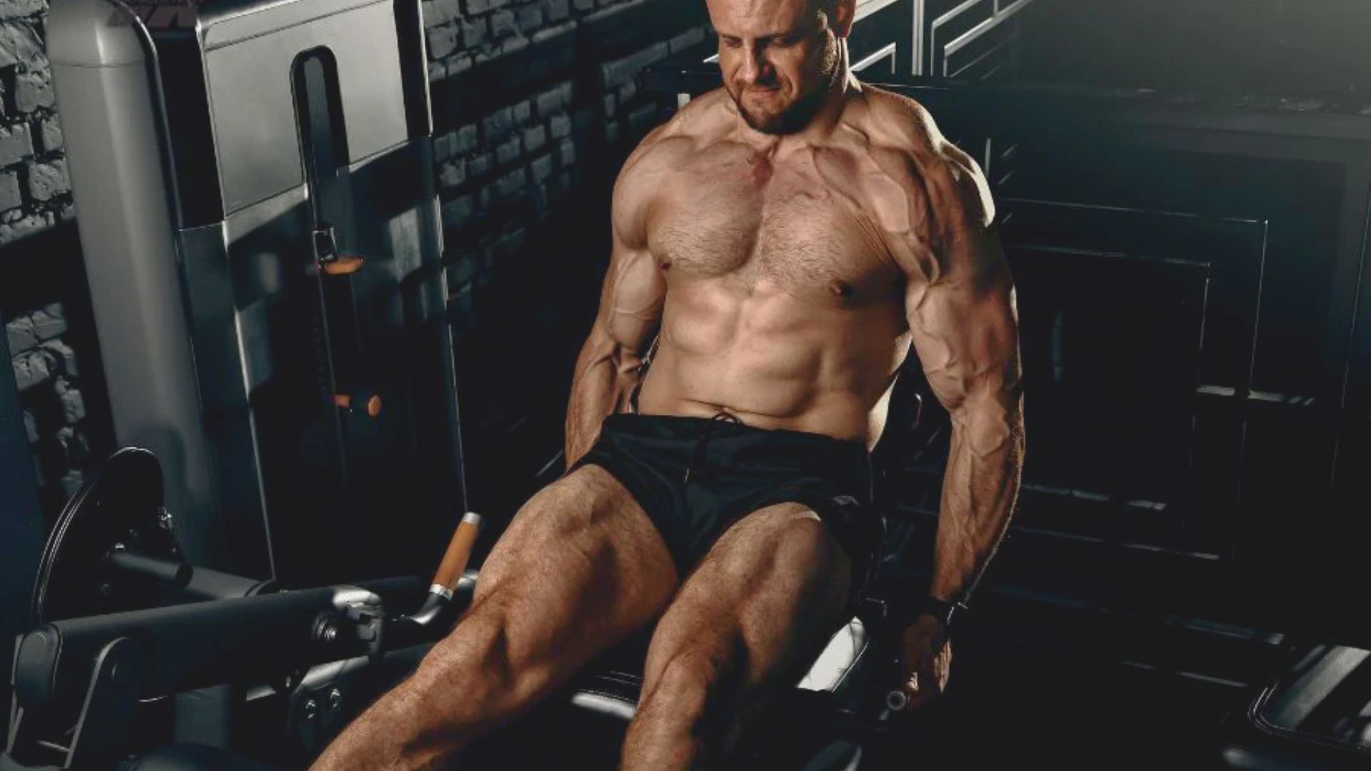 A man sits on a gym machine, focusing on his workout routine involving sets, reps, and progression strategy.