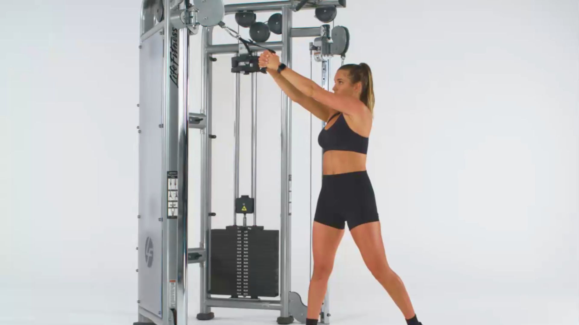 A woman exercises on a pull-up machine, focusing on her strength training routine in a gym setting.