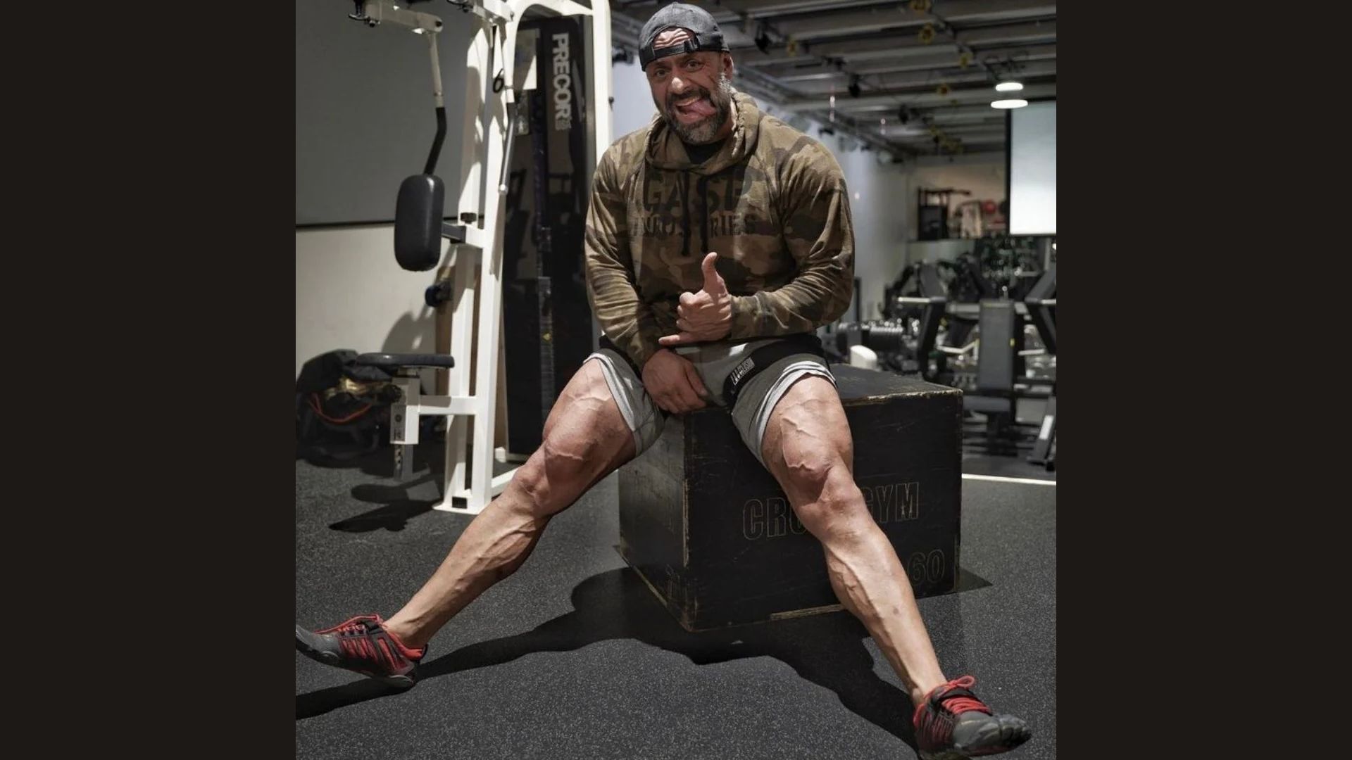 A man sitting on a gym bench, looking relaxed and focused, surrounded by exercise equipment.