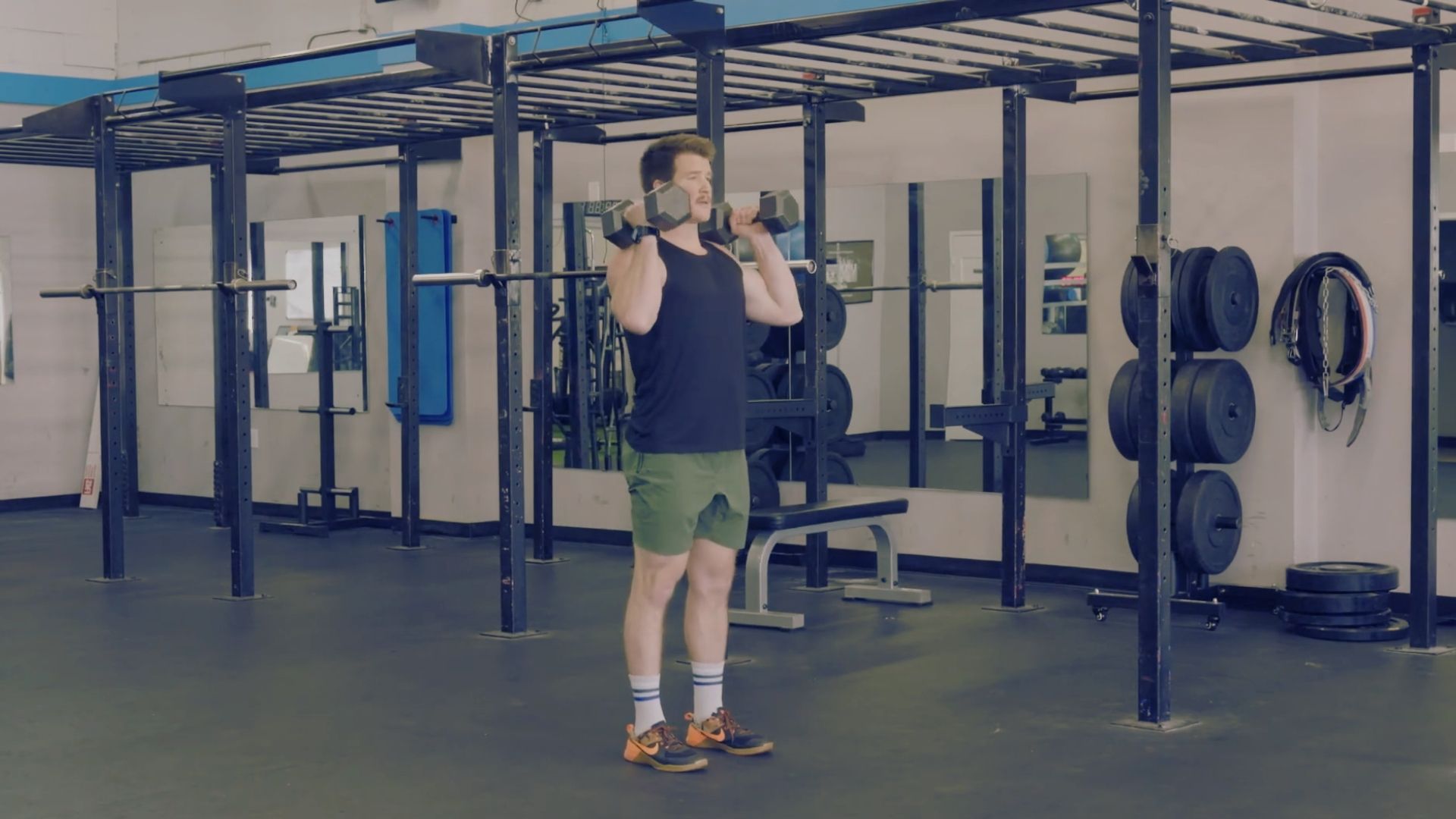 A man performs a squat in a gym, preparing to transition into a dumbbell power clean.
