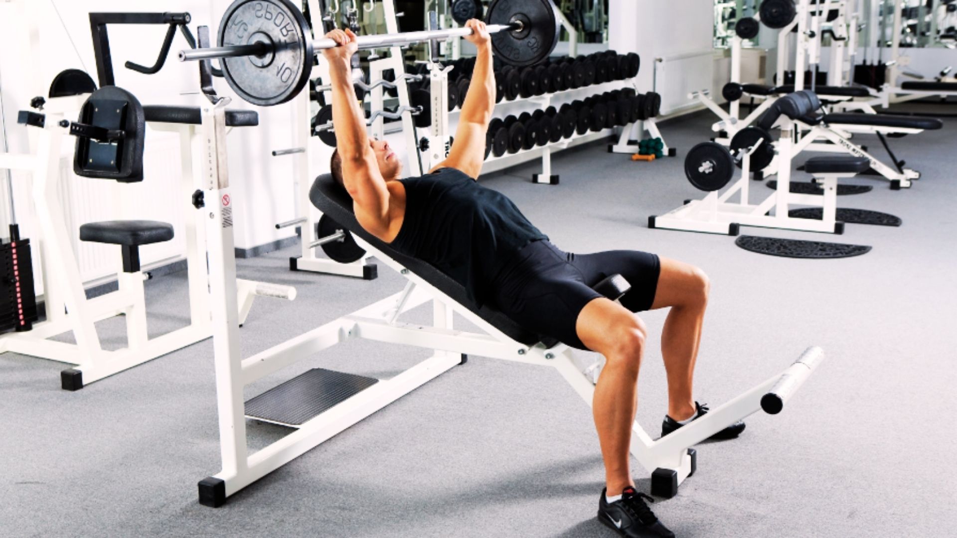A man is executing a bench press in a gym, concentrating on raising a barbell from his chest.