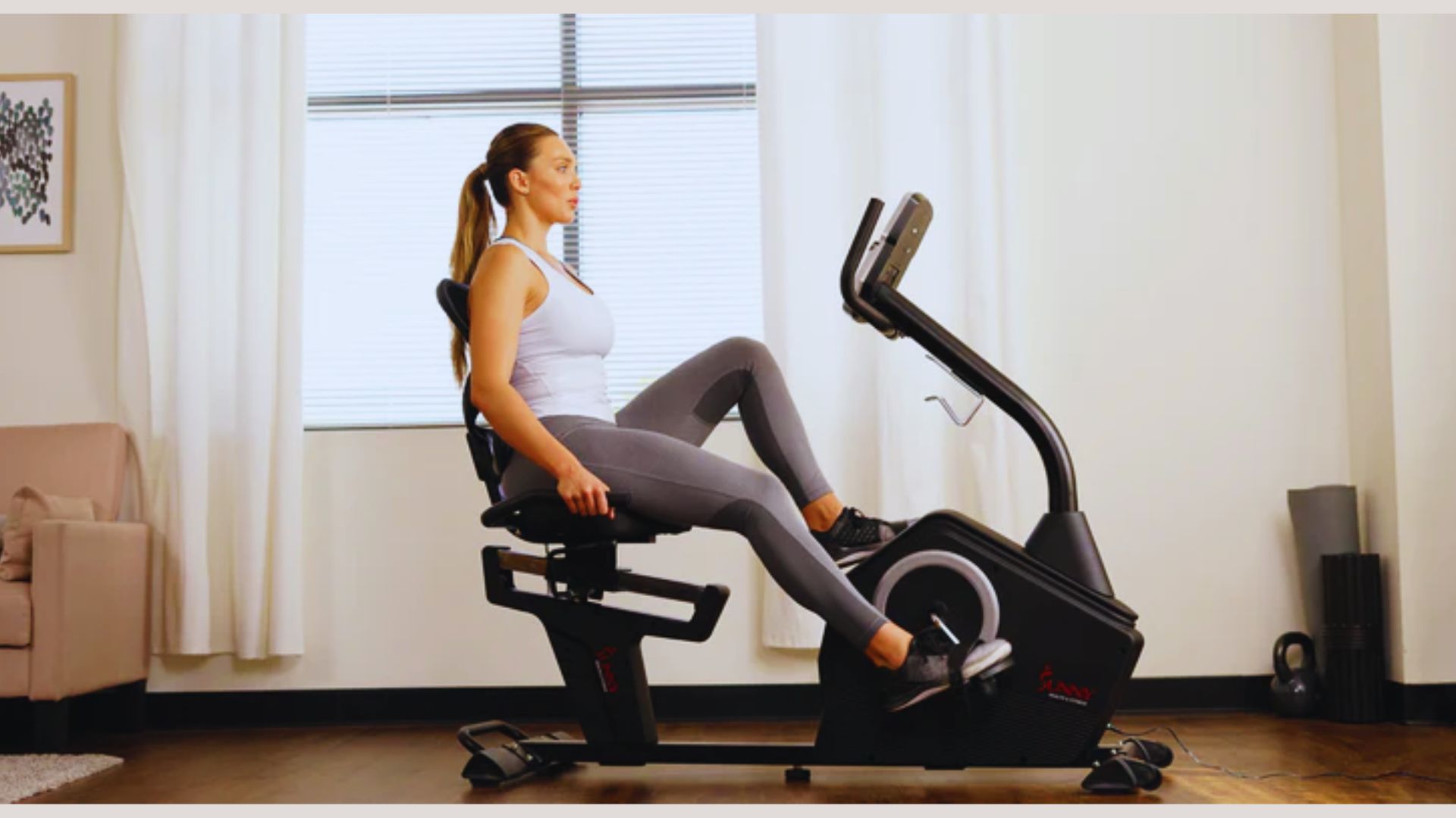 A woman is seated on a stationary bike, focused on her workout in a bright, well-lit gym environment.