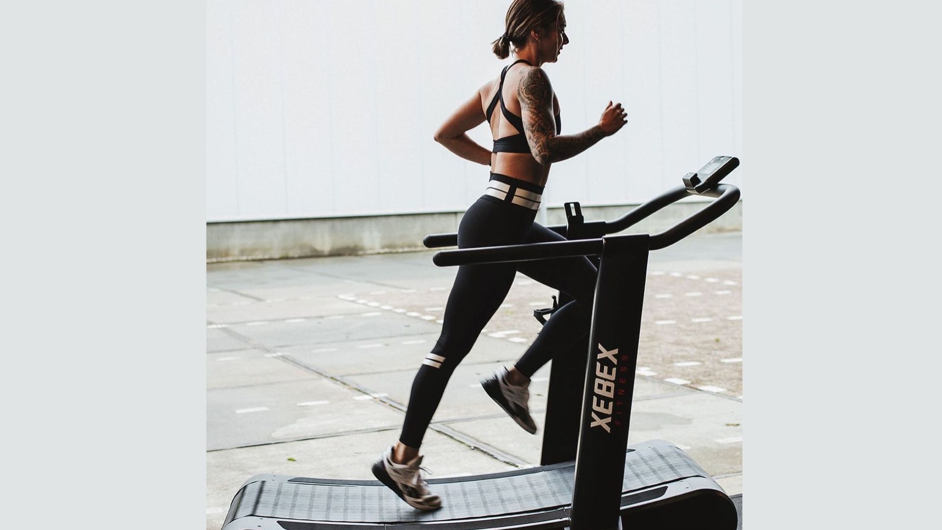 A woman is jogging on a treadmill in a gym, focused on her workout routine.