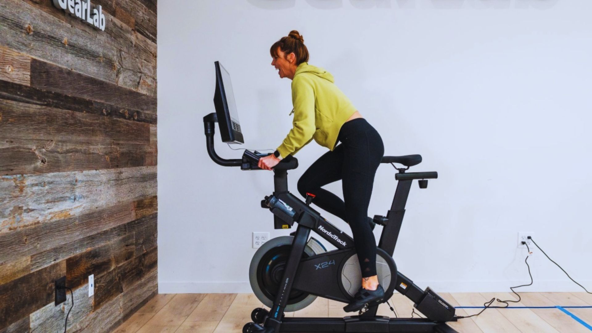 A woman is exercising on a stationary bike in a well-lit room, focused on her workout.