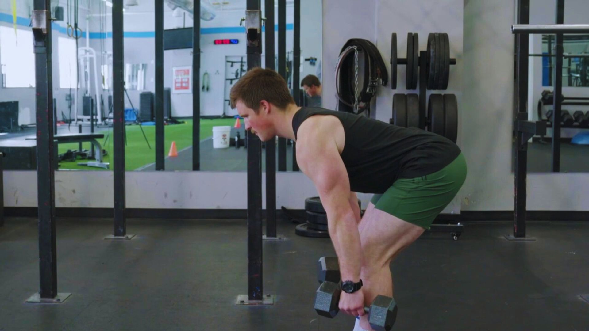 A man performs a squat while holding a dumbbell in his right hand, focusing on strength training.