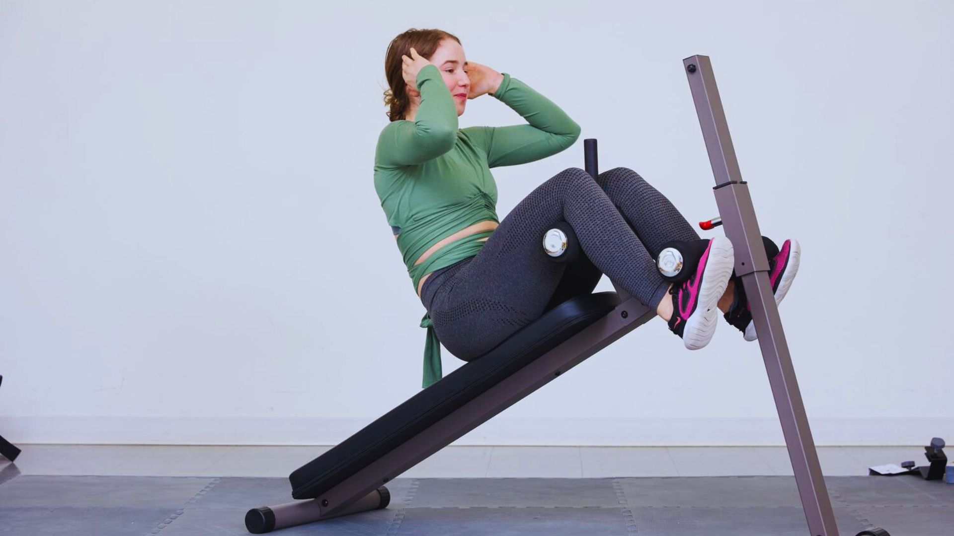 A woman sits on a gym bench, surrounded by various ab machines in the background.