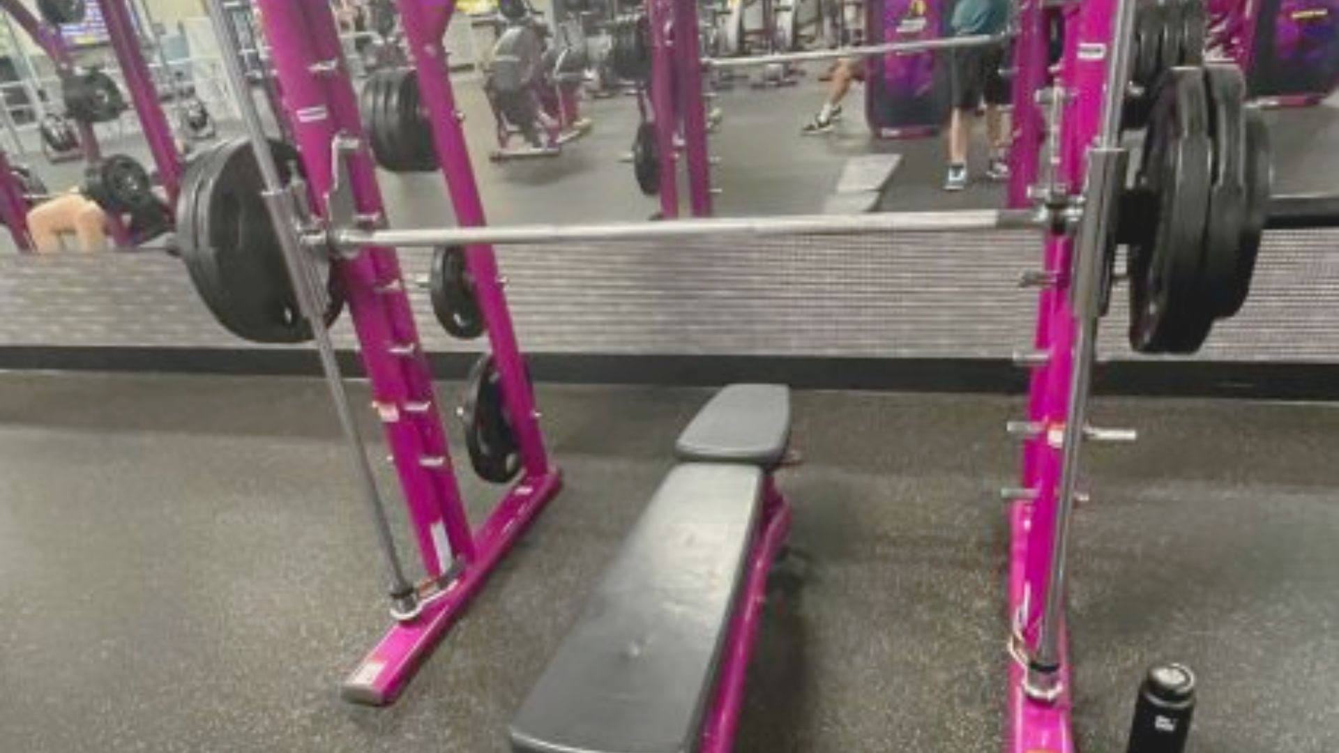 A pink smith machine positioned in a gym alongside a weight bench, showcasing a vibrant workout space.