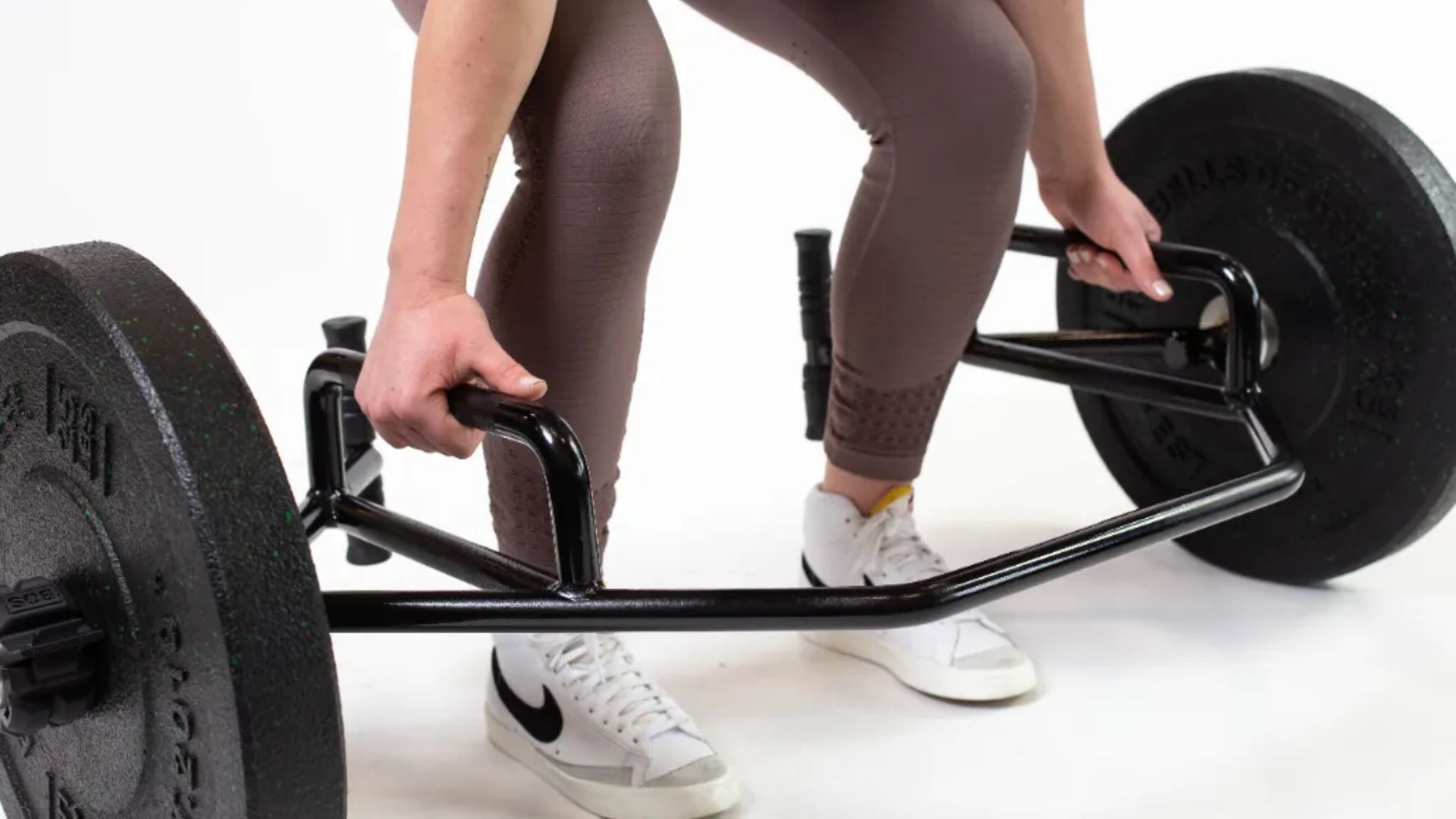 A woman performs a trap bar deadlift, lifting a barbell with proper form and focus in a gym setting.