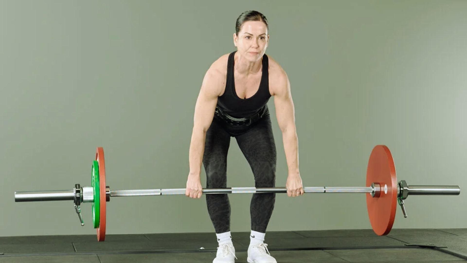 A woman lifts a barbell loaded with red and green plates, demonstrating strength training in a gym setting.
