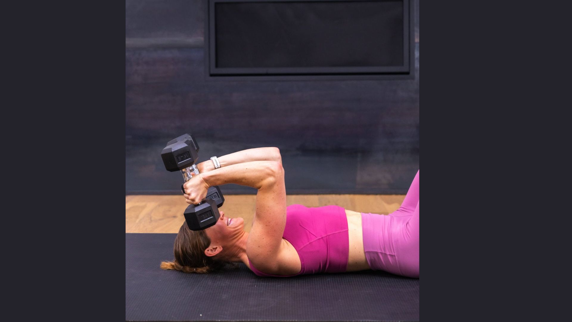 A woman performs a workout with a dumbbell, focusing on her form and strength, with a "REPEAT FOR REPS" sign nearby