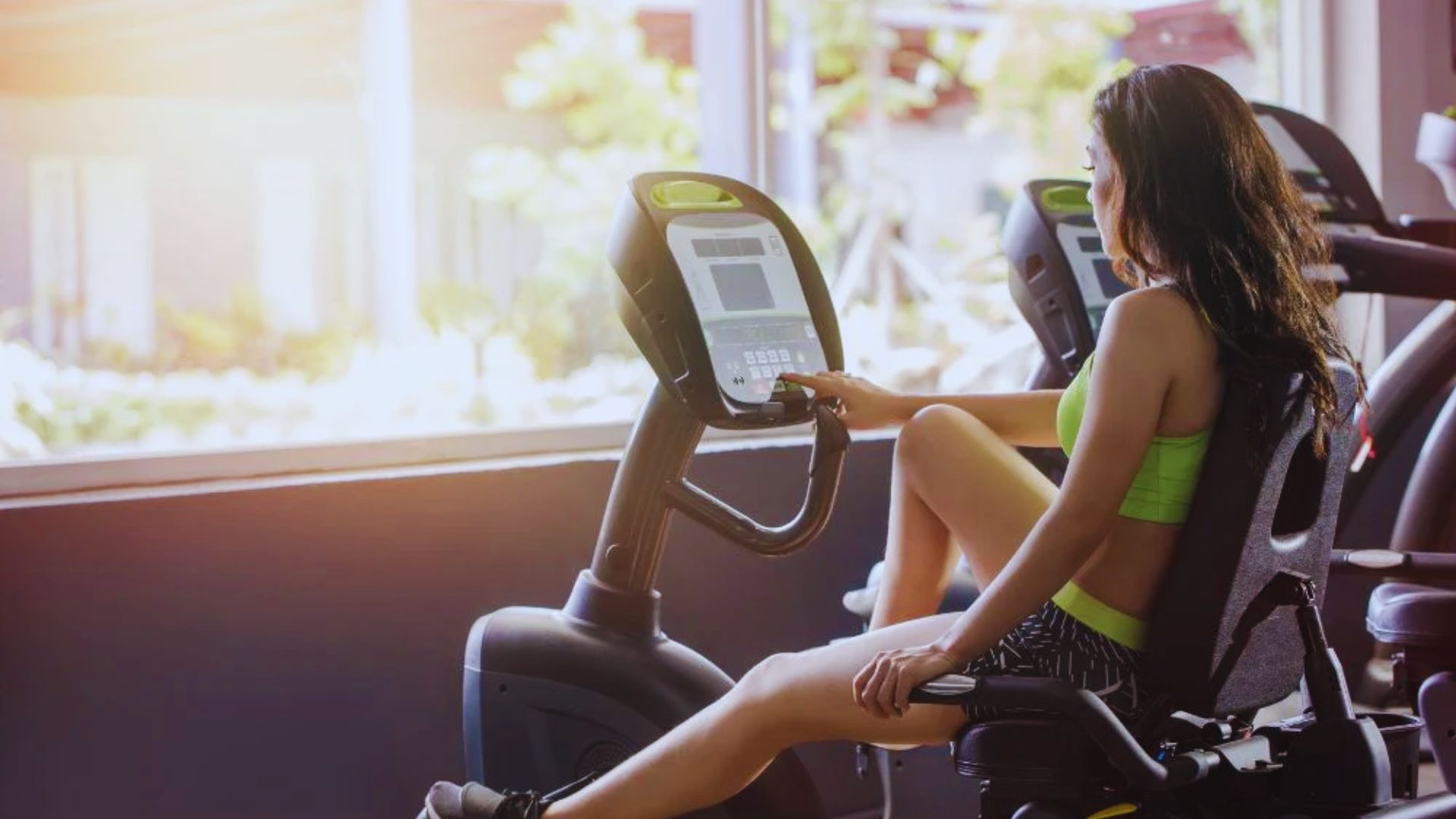 A woman is exercising on a stationary bike in a gym setting, focused on her workout.
