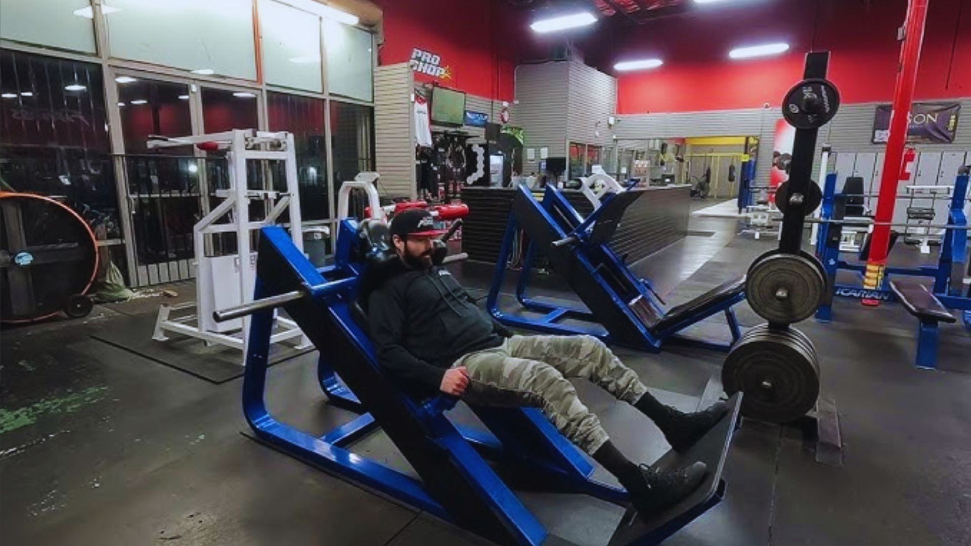 A man sits on a gym bench, appearing relaxed and focused in a fitness environment.