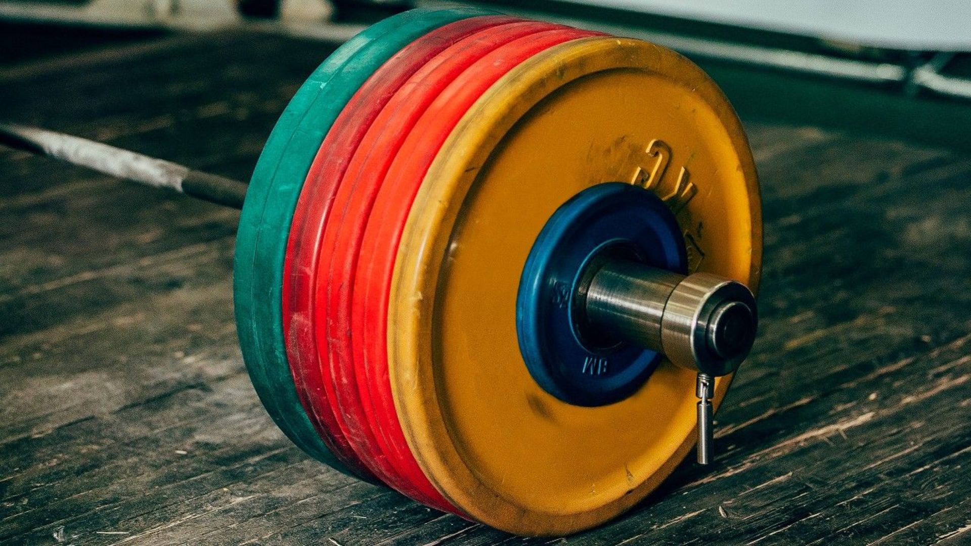 A colorful barbell rests on a wooden floor, illustrating strength training concepts for back off sets.