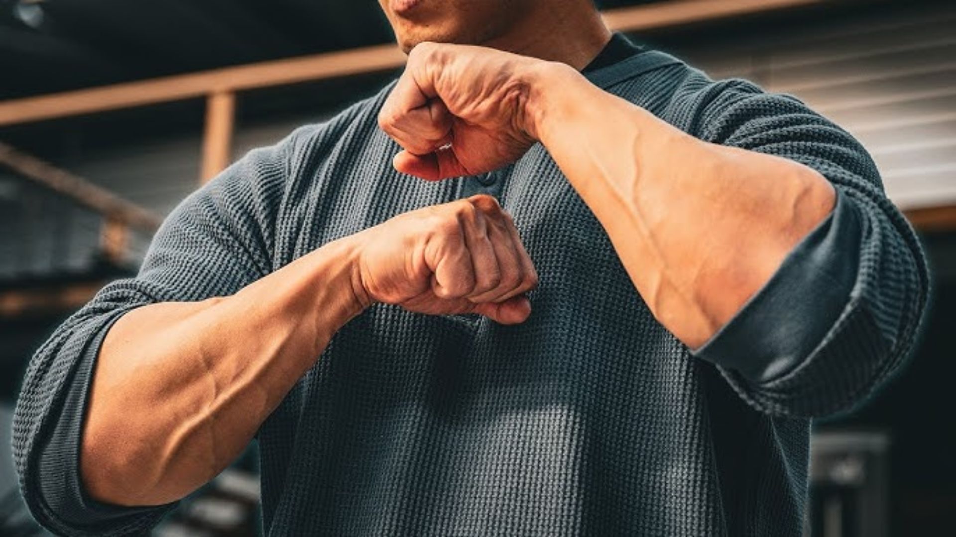 A man flexes his biceps in a gym, showcasing his muscular forearms and strong grip.