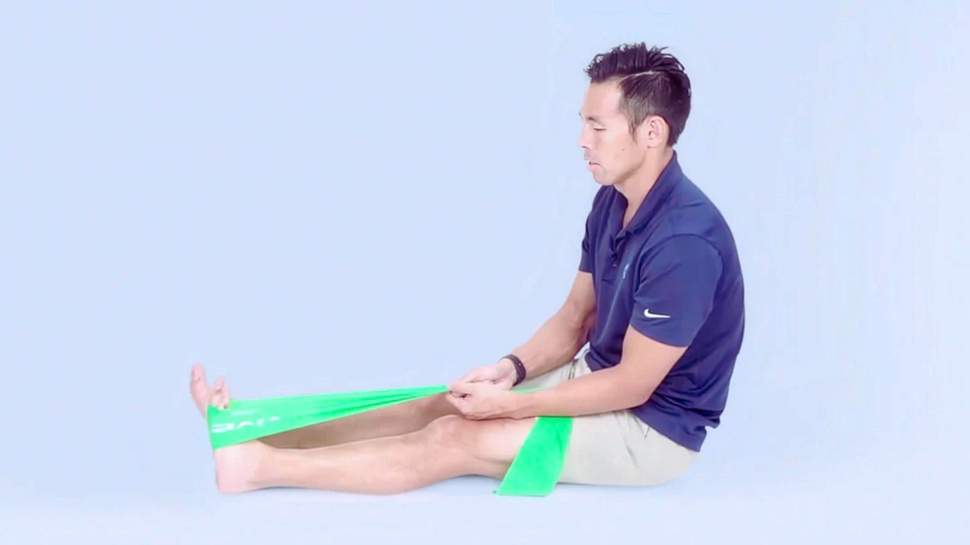 A man sits on the floor with a green band wrapped around his leg, appearing focused on an activity.