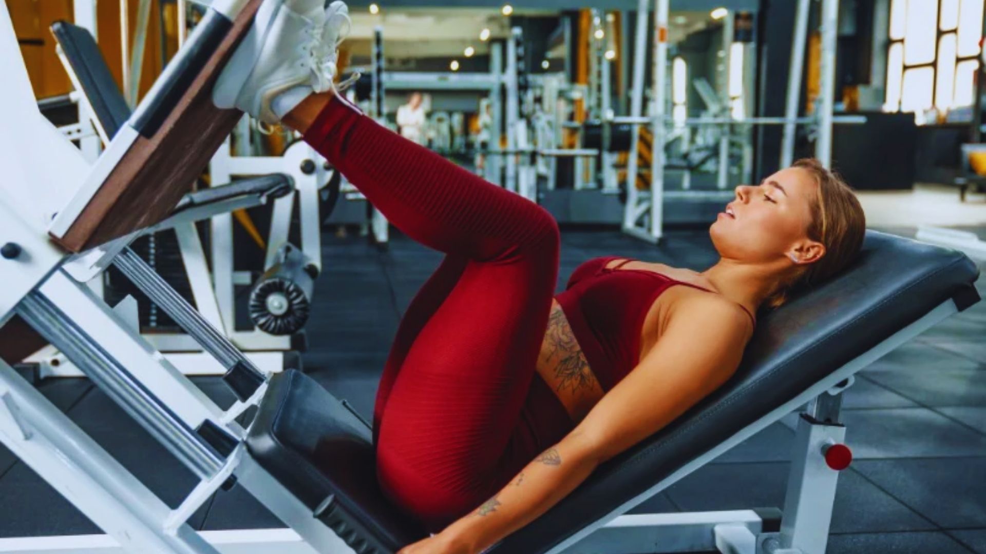A woman sits on a gym bench, demonstrating a slightly wider stance for exercise guidance.
