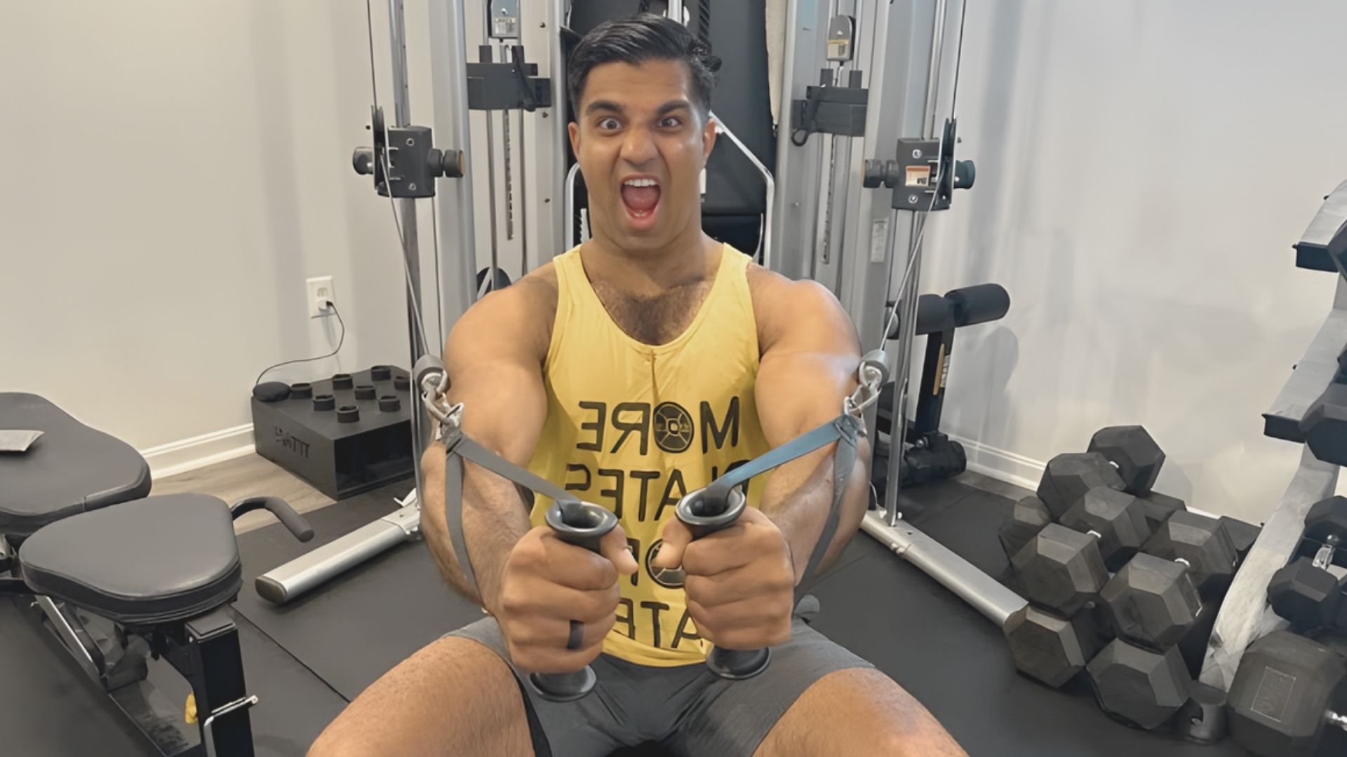 A man sits on a gym bench with his arms extended outward, preparing for a workout or stretch.