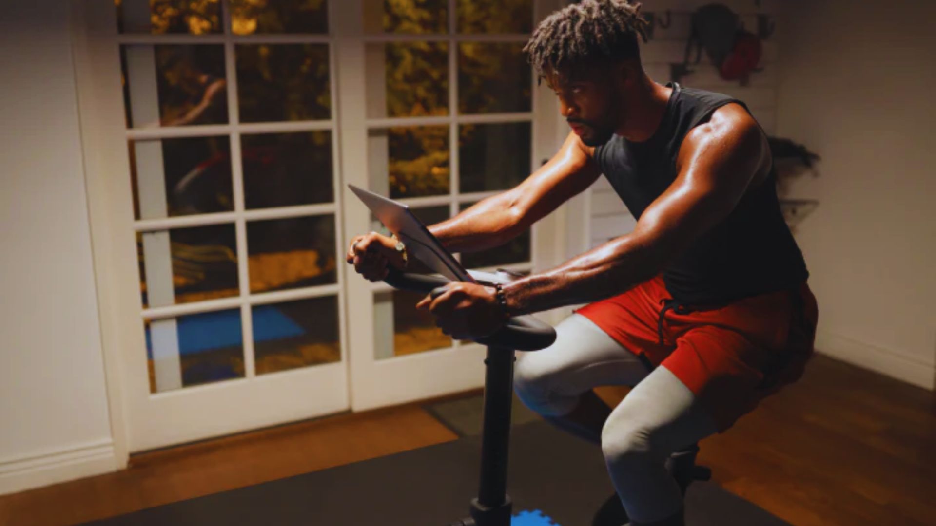A man is exercising on a stationary bike in a well-lit room, focused on his workout.