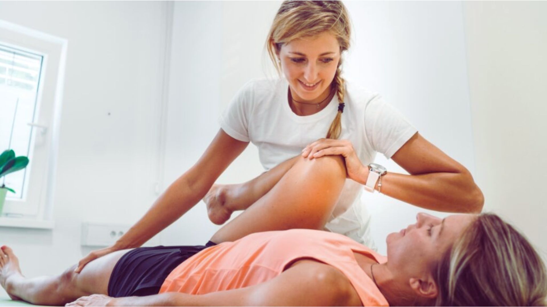 A woman receives a leg stretch from a physical therapist in a clinical setting, focusing on rehabilitation and mobility.
