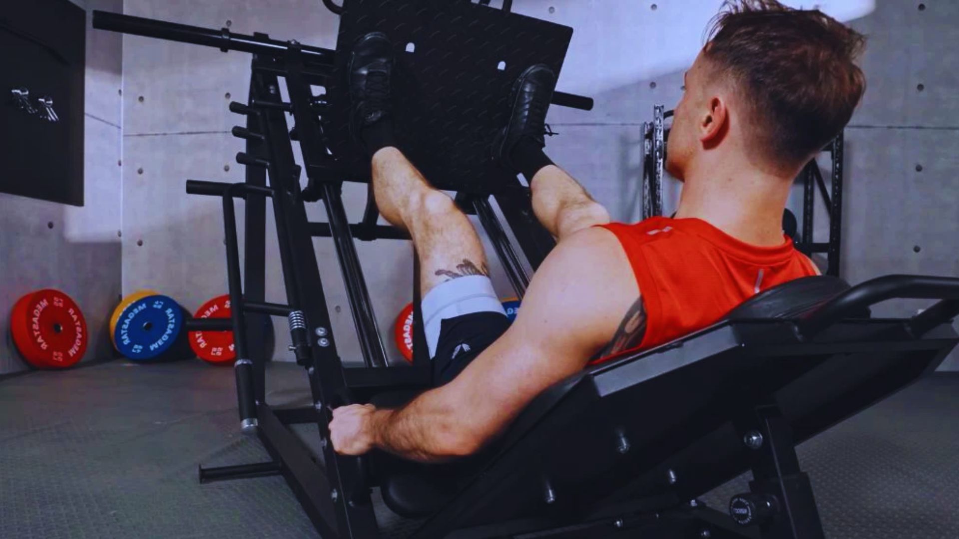 A man sits on a gym machine, focusing on his workout technique, emphasizing pushing through his heels.