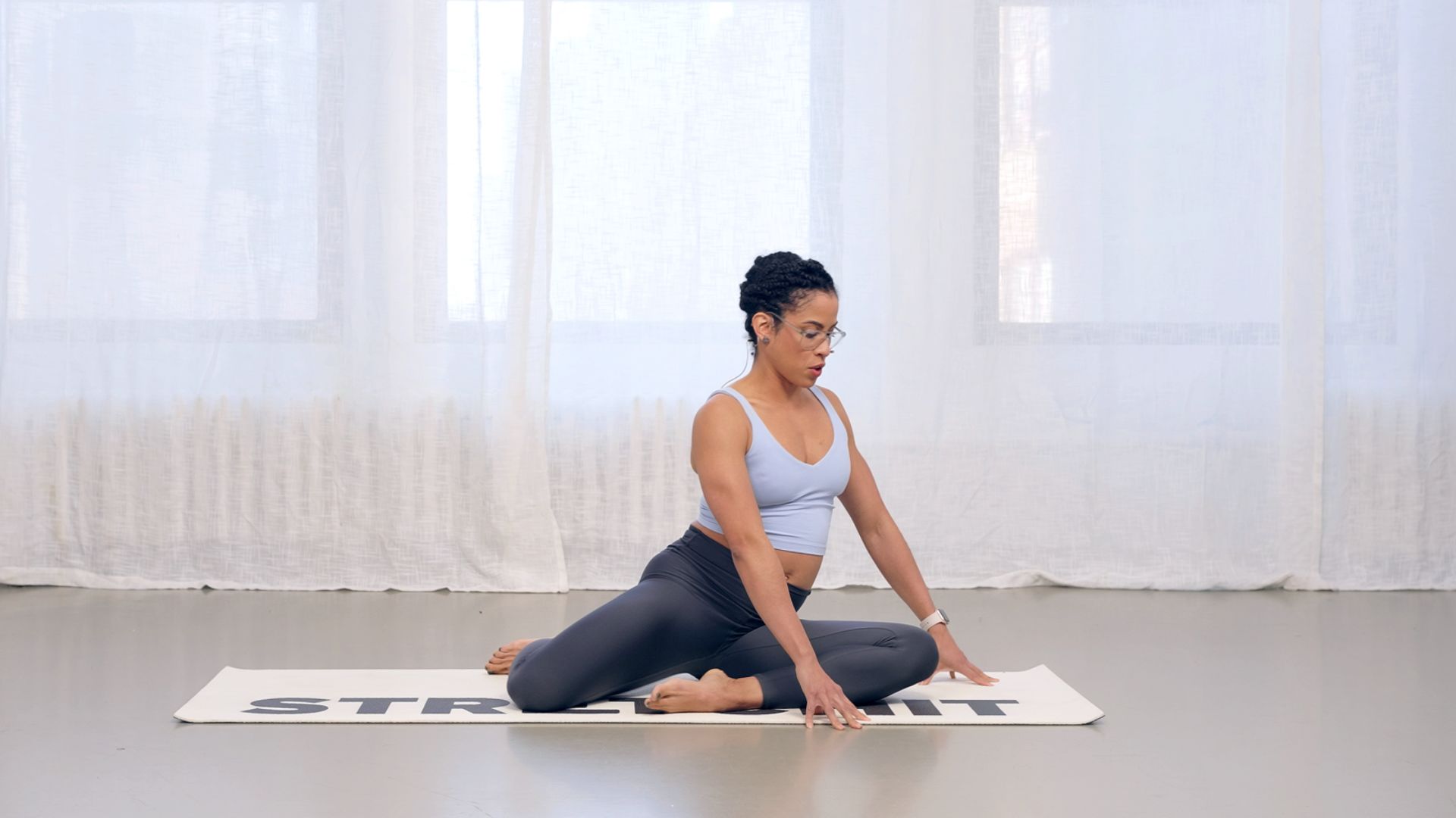 2. A woman practices yoga on a mat, sitting peacefully with her eyes closed in a calm and tranquil setting.