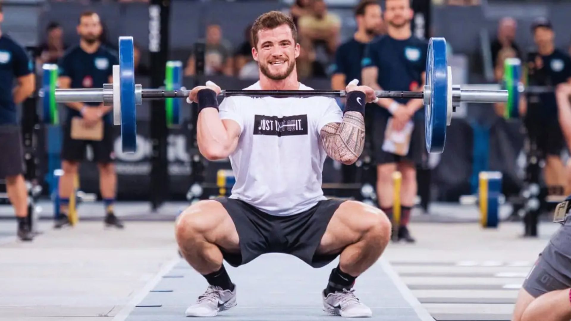 A man performs a squat with a barbell at a CrossFit competition, demonstrating athleticism and determination.