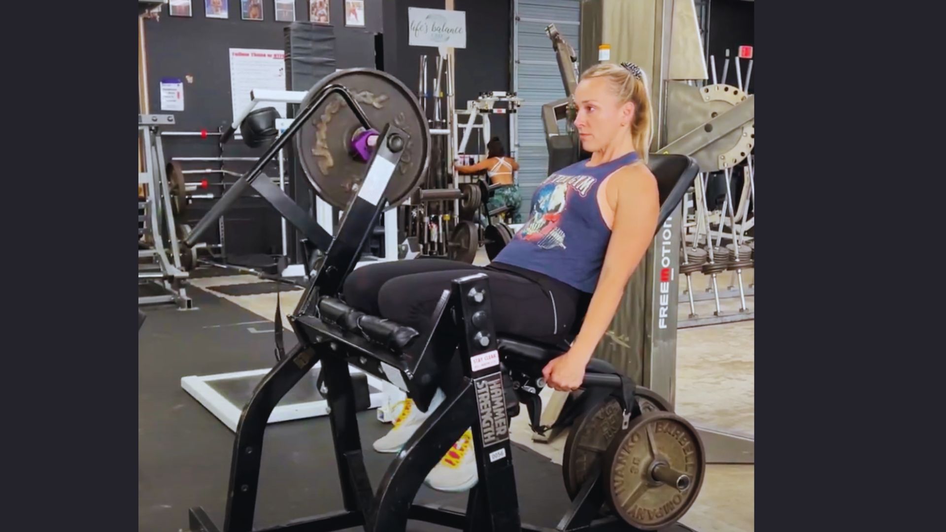 A woman is seated on a gym machine, engaged in Hammer curl exercise