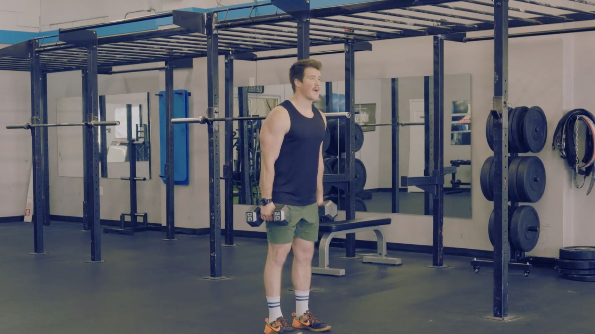 In a gym, a man squats on a barbell, poised to begin a power clean exercise from this starting position.